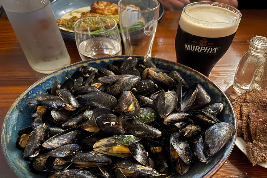 Close-up of a dish of mussels with a glass of Murphy's stout behind it